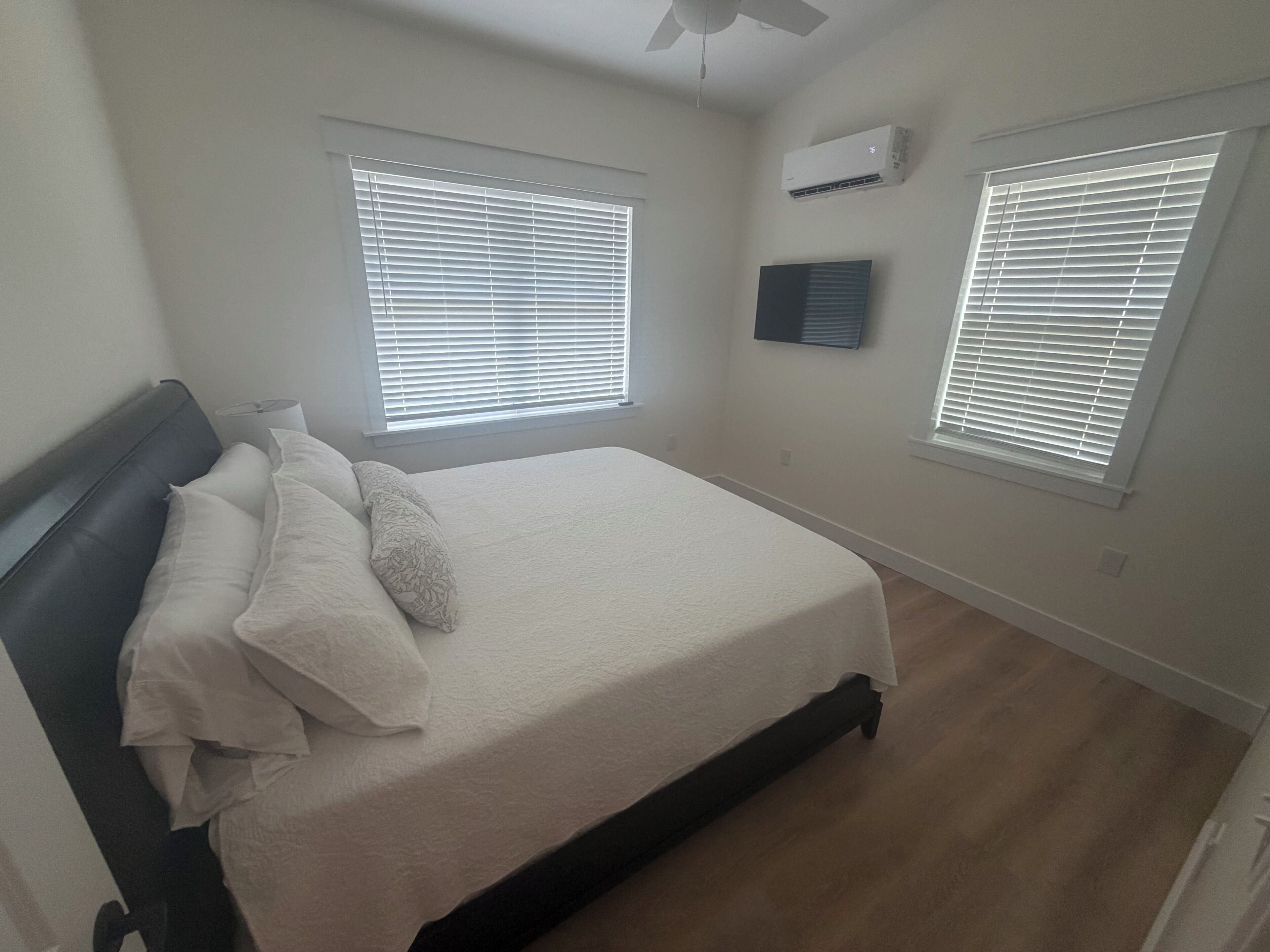 Une chambre à coucher comprenant un lit, deux fenêtres équipées de stores, un climatiseur et un ventilateur de plafond.