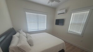 Un dormitorio con cama, dos ventanas con persianas, un equipo de aire acondicionado y un ventilador de techo.