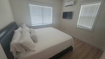 Une chambre à coucher comprenant un lit, deux fenêtres équipées de stores, un climatiseur et un ventilateur de plafond.