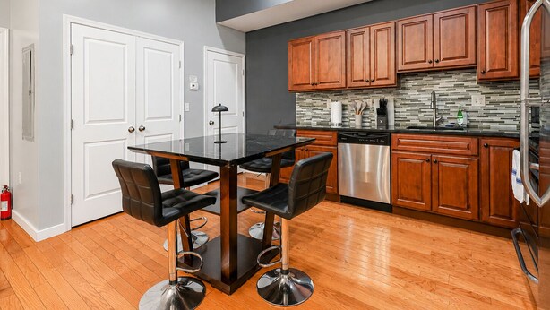 A modern kitchen with wooden cabinets, a stainless steel dishwasher, and a black marble countertop. - The Camac Hideaway - 2BR near Convention Center (Philadelphia)