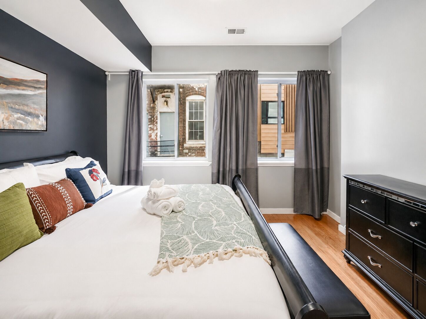 Een moderne slaapkamer met een groot bed, een dressoir en uitzicht op een bakstenen gebouw door een raam.