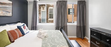 Un dormitorio moderno con una cama grande, un aparador y vistas a un edificio de ladrillo a través de una ventana.