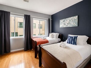 Ein Hotelzimmer mit zwei Betten, einem großen Fenster, einer dunklen Wand und einem Gemälde.