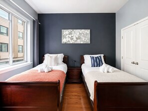 Ein Hotelzimmer mit zwei Holzbetten, einer dunklen Wand, einem Fenster und einem Gemälde.