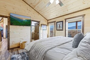 Ein Interieur einer Holzhütte mit Bett, Fernseher und Fenster mit Blick auf die Berge.