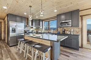 Uma cozinha moderna com uma ilha grande, banquetas, eletrodomésticos de aço inoxidável e vista para o exterior.