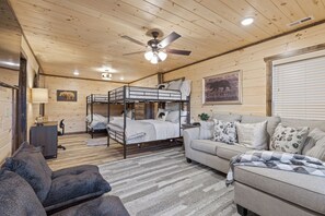 Een kamer in chaletstijl met stapelbedden, een slaapbank en een plafondventilator.