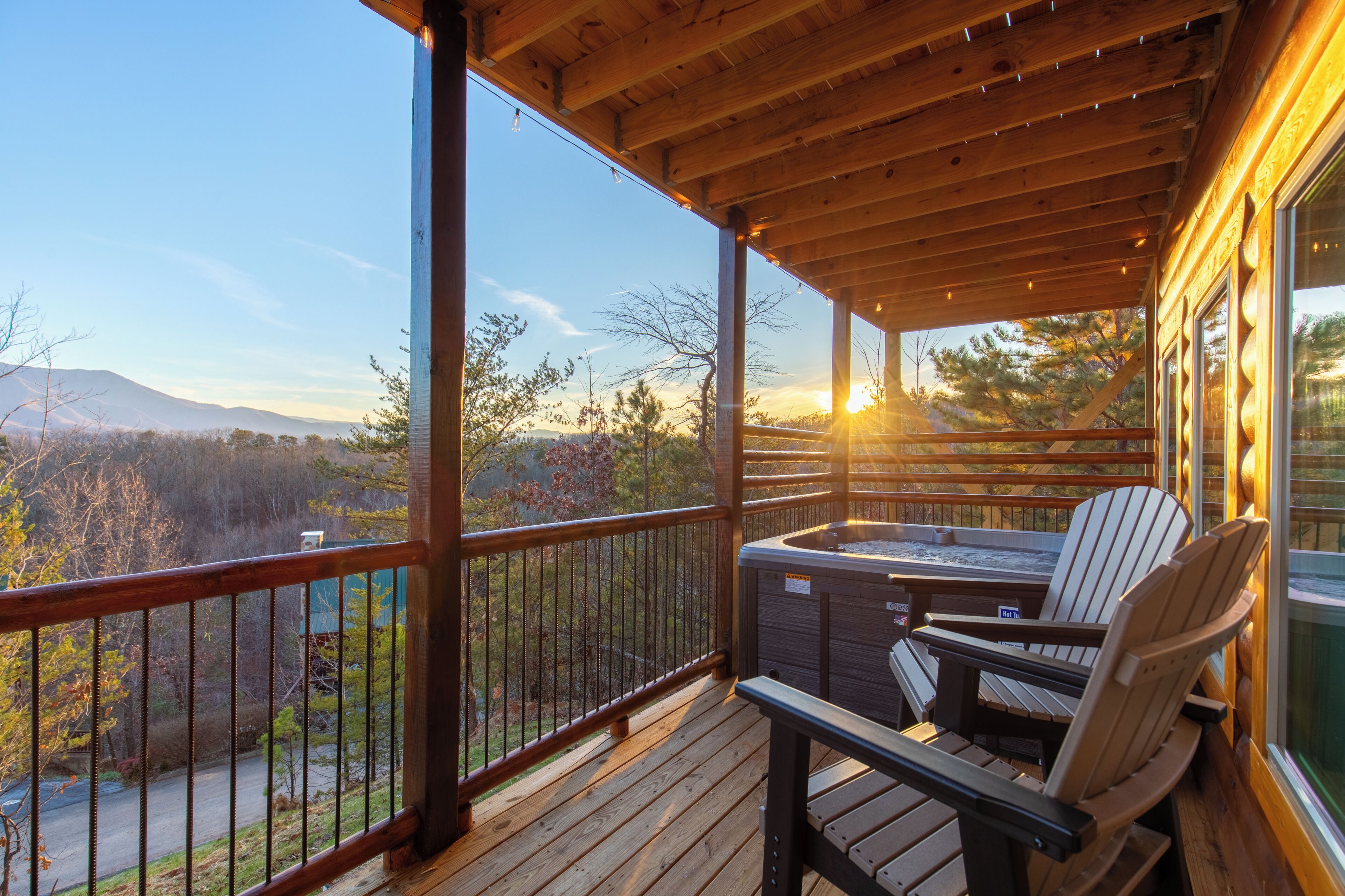 A wooden deck with a hot tub and chairs, overlooking a mountainous landscape.