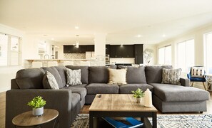 A modern living room with a sectional sofa, a coffee table, and a dining area in the background. - Oceanview 5-bedroom house for 12 people in Federal Way perfect for family stays (Federal Way)