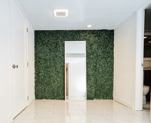 Ein Flur mit einer grünen Wand aus Blättern, einer weißen Tür und einem gefliesten Boden.