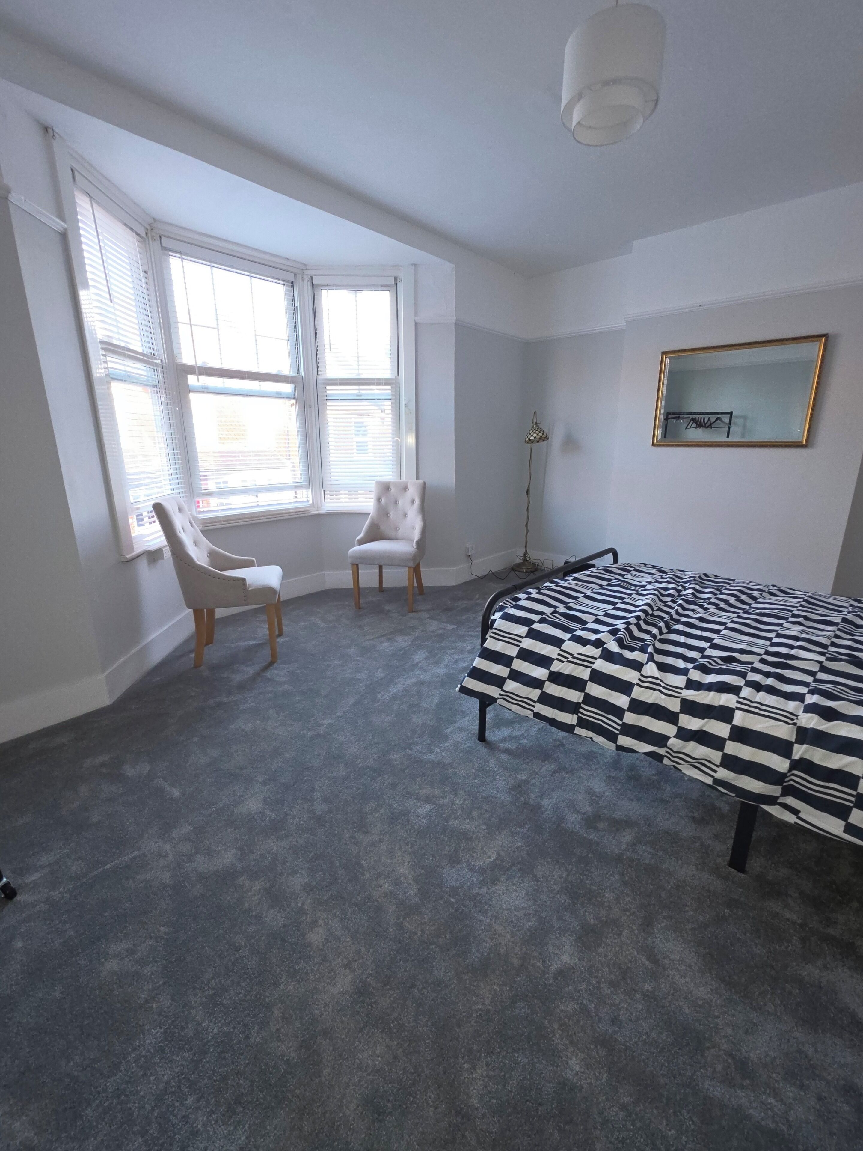A bedroom with a bed, a chair, a floor lamp, and a window.