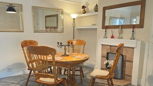 Un comedor con una mesa redonda de madera, cuatro sillas, una lámpara colgante negra y una chimenea con repisa.