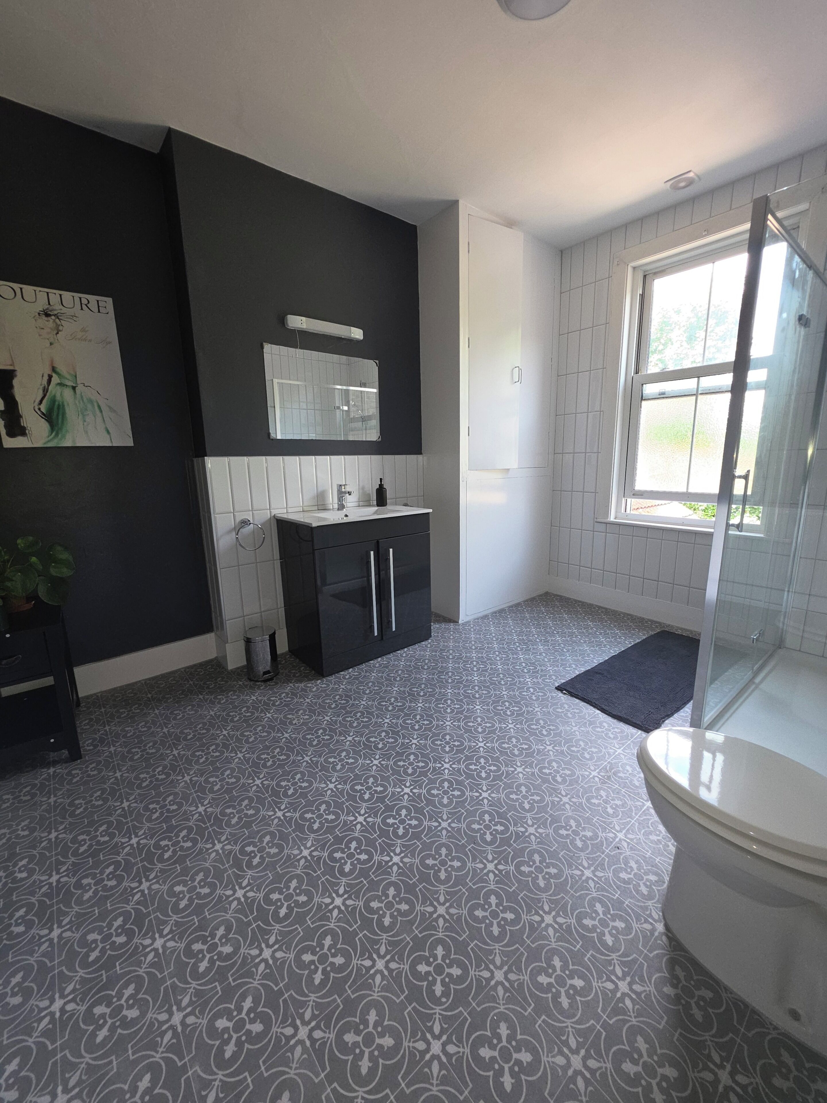 Un baño con piso de baldosas blanco y negro, un lavamanos blanco, un mueble de tocador oscuro, un espejo y una ventana.