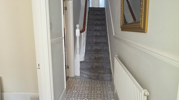 Un pasillo con suelo estampado, una escalera, un radiador y un espejo en la pared.