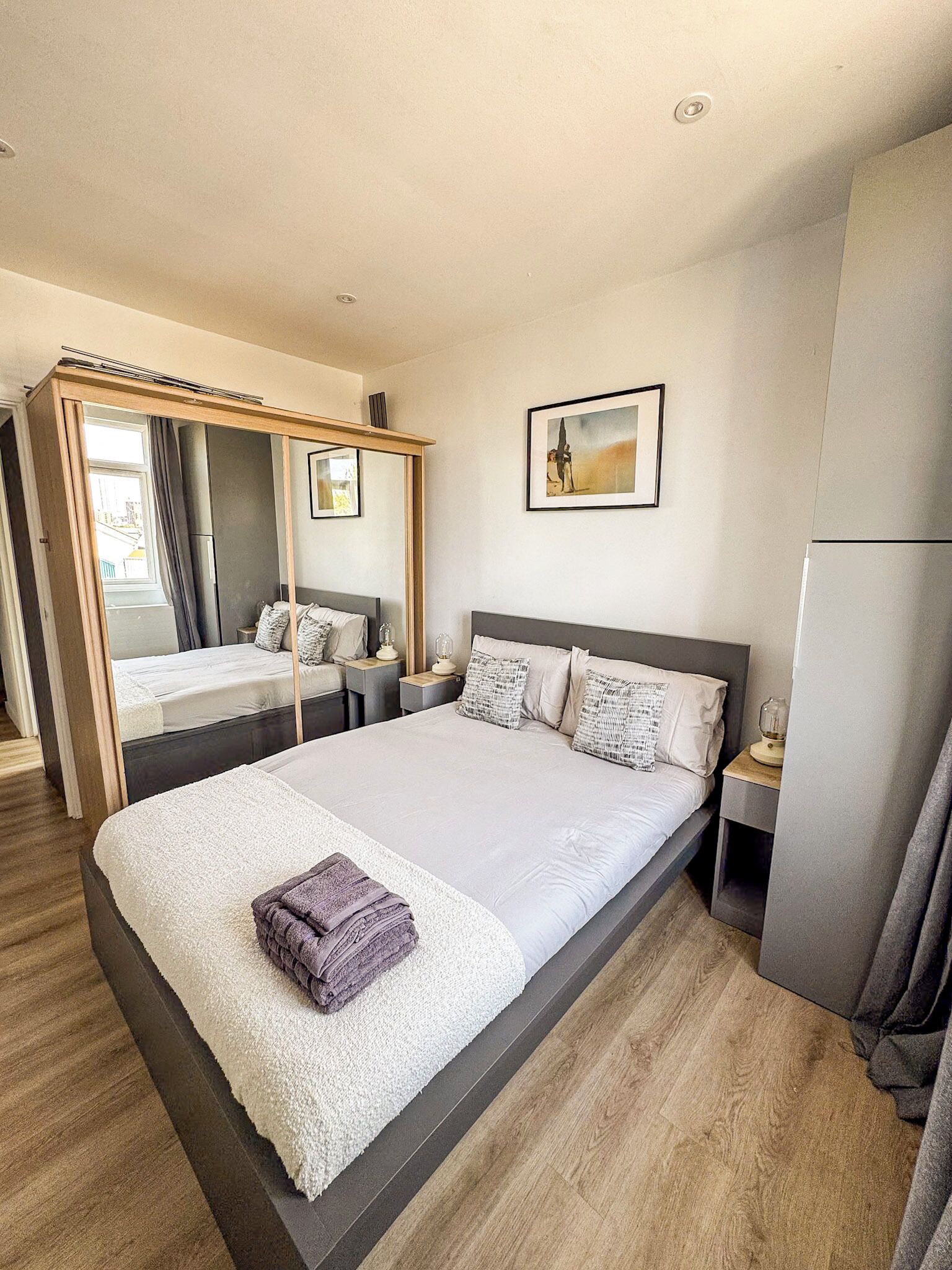 A hotel room with a large bed, a bedside table, a mirror, a picture on the wall, and a wardrobe.