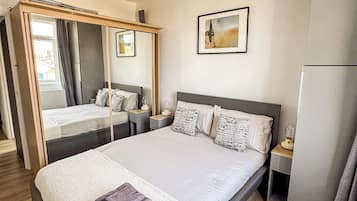 A hotel room with a large bed, a bedside table, a mirror, a picture on the wall, and a wardrobe.