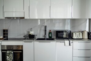 A modern kitchen with white cabinets, a stainless steel oven, a microwave, a toaster, and a sink with a faucet. - Modern 2 Bedroom Apartment - 16 Minutes to Central London (London)