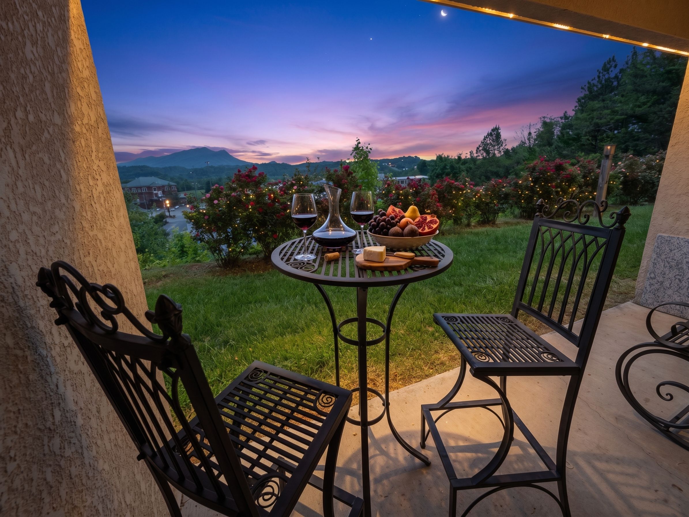 An outdoor patio with a round table, two chairs, and a view of a mountain range at dusk.