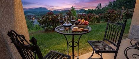 An outdoor patio with a round table, two chairs, and a view of a mountain range at dusk.