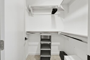 Een witte kamer met een deur, een inbouwkast met planken en een klein zithoekje.