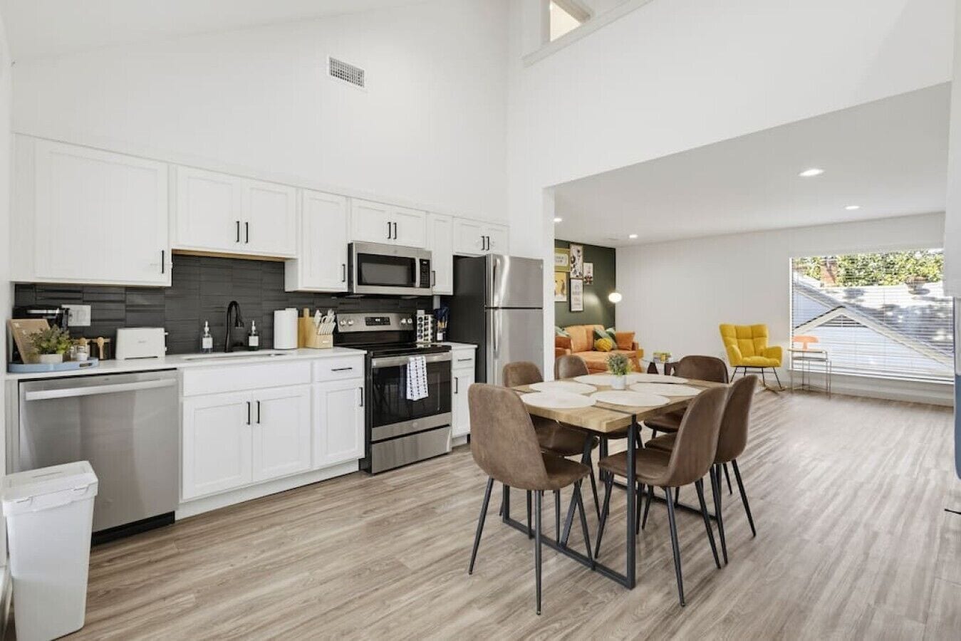 A modern kitchen with white cabinets, stainless steel appliances, and a dining area with a wooden table and chairs.