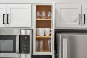 Eine Küche mit weißen Schränken, einer Mikrowelle, einem Kühlschrank und einem integrierten Weinkühlschrank mit Gläsern und Tassen.