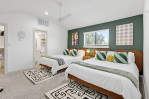 Ein Schlafzimmer mit zwei Betten, einem Deckenventilator, einem Fenster mit Jalousien und Bildern an der Wand.