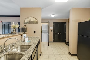 A kitchen with granite countertops, stainless steel sink, and a black refrigerator.