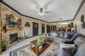 A spacious living room with a fireplace, a large sofa, and a television mounted on the wall.
