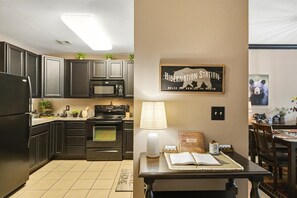A kitchen with dark cabinets, a stove, and a microwave. There's a sign on the wall that reads 'Hibernation Station.'