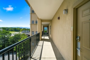 A corridor with a balcony, a door with a keypad lock, and a view of greenery and buildings.