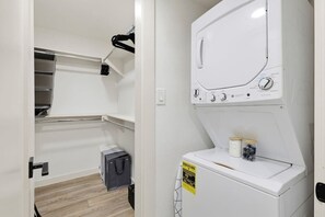 Ein Waschraum mit nebeneinander gestapelten Waschmaschine und Trockner, einem kleinen Stauraumschrank und einer Regaleinheit.