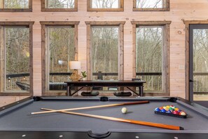 Ein Billardtisch mit Spielstöcken und Kugeln, eine Lampe und ein Tisch mit Blick durch große Fenster.