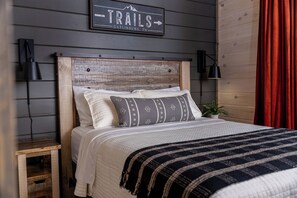 A bed with a wooden headboard, two bedside lamps, a sign above the bed, and a red curtain. - Mountain Explorers Retreat (Gatlinburg)