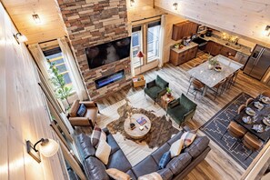 A modern interior with a stone fireplace, a flat-screen TV, a dining area, and a cozy seating area with leather sofas and a patterned rug. - Sleeps 16, Private Heated Indoor Pool, Theater, 1 Mi to Downtown Gatlinburg (Gatlinburg)