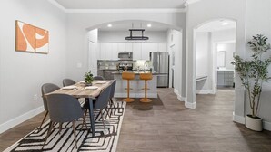 A modern kitchen with stainless steel appliances, a dining area with a wooden table and chairs, and a hallway leading to another room. - Sleeps 5 | Downtown & Sport Stadiums Nearby | Pool + Gym + Free Parking (Houston)