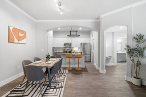 Eine moderne Küche mit Edelstahlgeräten, ein Essbereich mit Holztisch und Stühlen sowie ein Flur zu einem weiteren Zimmer.
