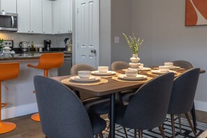 A dining area with a table set for four, surrounded by chairs, in a modern kitchen with white cabinets and a microwave. - Sleeps 5 | Downtown & Sport Stadiums Nearby | Pool + Gym + Free Parking (Houston)