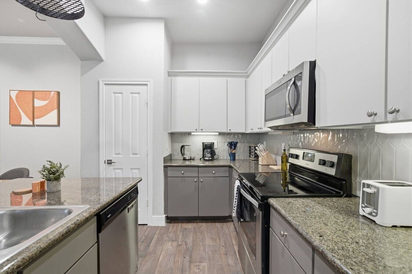 A modern kitchen with stainless steel appliances, white cabinetry, and a granite countertop.