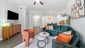 A modern living room with a sofa, armchair, coffee table, and a TV. - Sleeps 5 | Downtown & Sport Stadiums Nearby | Pool + Gym + Free Parking (Houston)