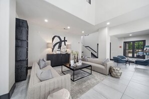 A spacious living area with a sofa set, a coffee table, and a dark wood cabinet. There is a staircase leading to an upper level, and a large window providing a view outside. - Sleeps 5 | Downtown & Sport Stadiums Nearby | Pool + Gym + Free Parking (Houston)
