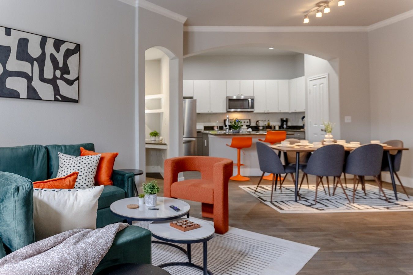 Ein modernes Wohnzimmer mit Sofa, Couchtisch und orangefarbenem Sessel. Im Hintergrund ist eine Essecke mit Tisch und Stühlen zu sehen.