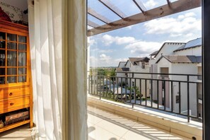A balcony with a view of a residential area, a wooden cabinet, and a window with curtains. - Spacious Two Bed Apartment with Loft (Midrand)