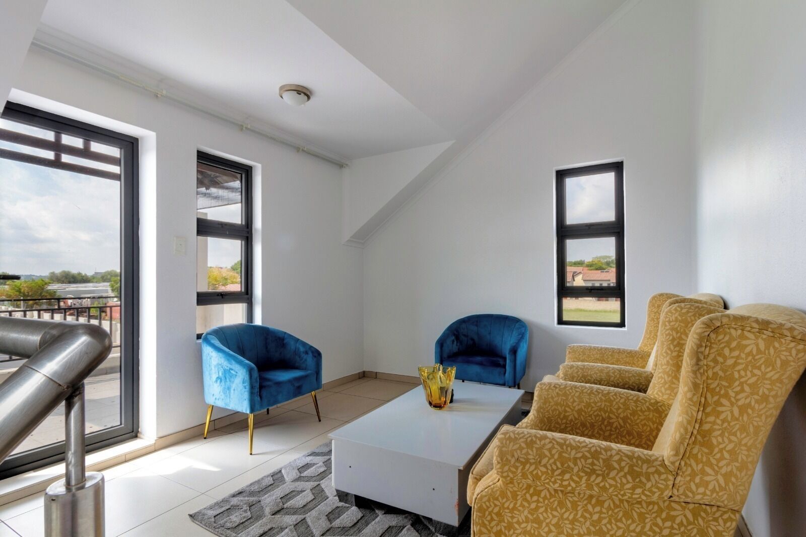 A modern living room with a white coffee table, two blue armchairs, and a yellow patterned sofa.