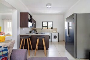 A modern kitchen with a built-in washing machine, a refrigerator, and a dining area with stools. - Spacious Two Bed Apartment with Loft (Midrand)