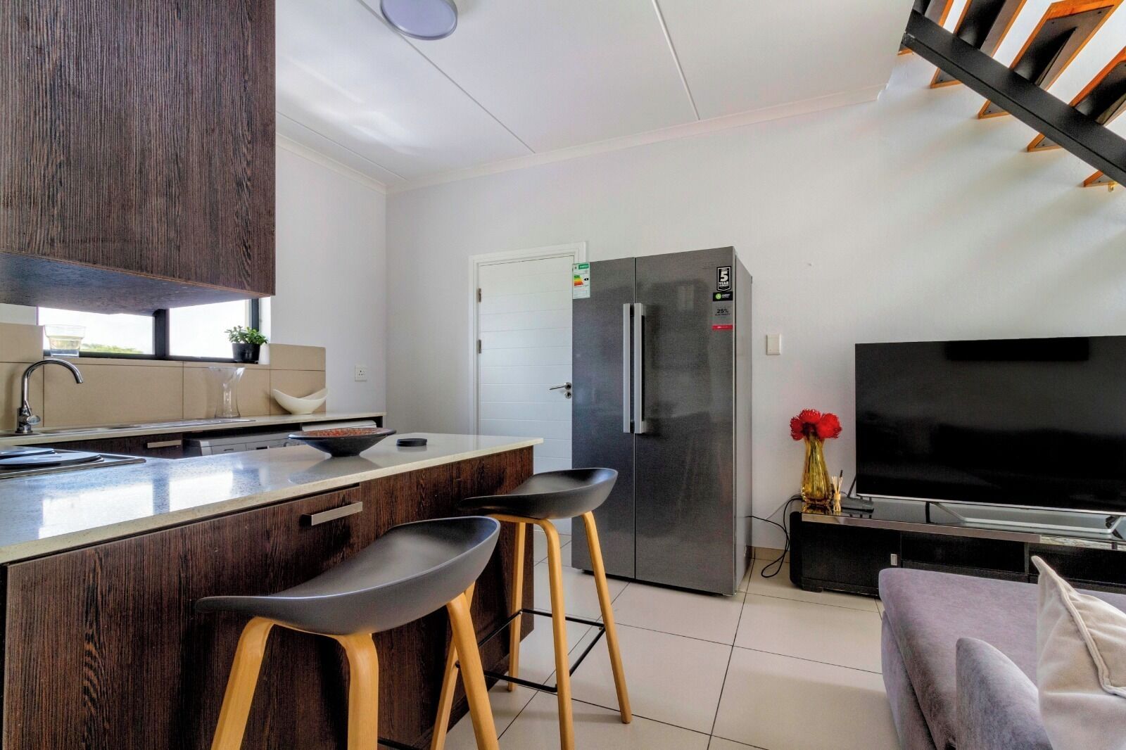 Een moderne keuken met een centraal eiland, barkrukken, een koelkast en een flatscreen televisie.