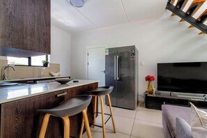 Eine moderne Küche mit Kochinsel, Barhocker, Kühlschrank und Flachbildfernseher.
