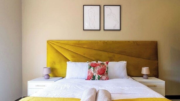 Ein Hotelzimmer mit einem Bett, zwei Nachttischen, einem Kopfteil und zwei gerahmten Bildern an der Wand.