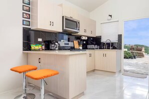A modern kitchen with a built-in microwave, coffee maker, and a small island with stools. - Sunset@ArecaHomes ~ Beach Access~Pool & Water Park (Discovery Bay, St Ann)