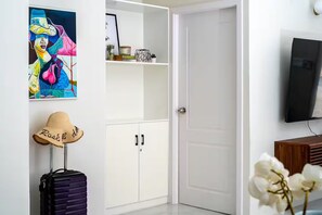 A room with a white wardrobe, a television, a suitcase, a hat, and a painting. - Sunset@ArecaHomes ~ Beach Access~Pool & Water Park (Discovery Bay, St Ann)